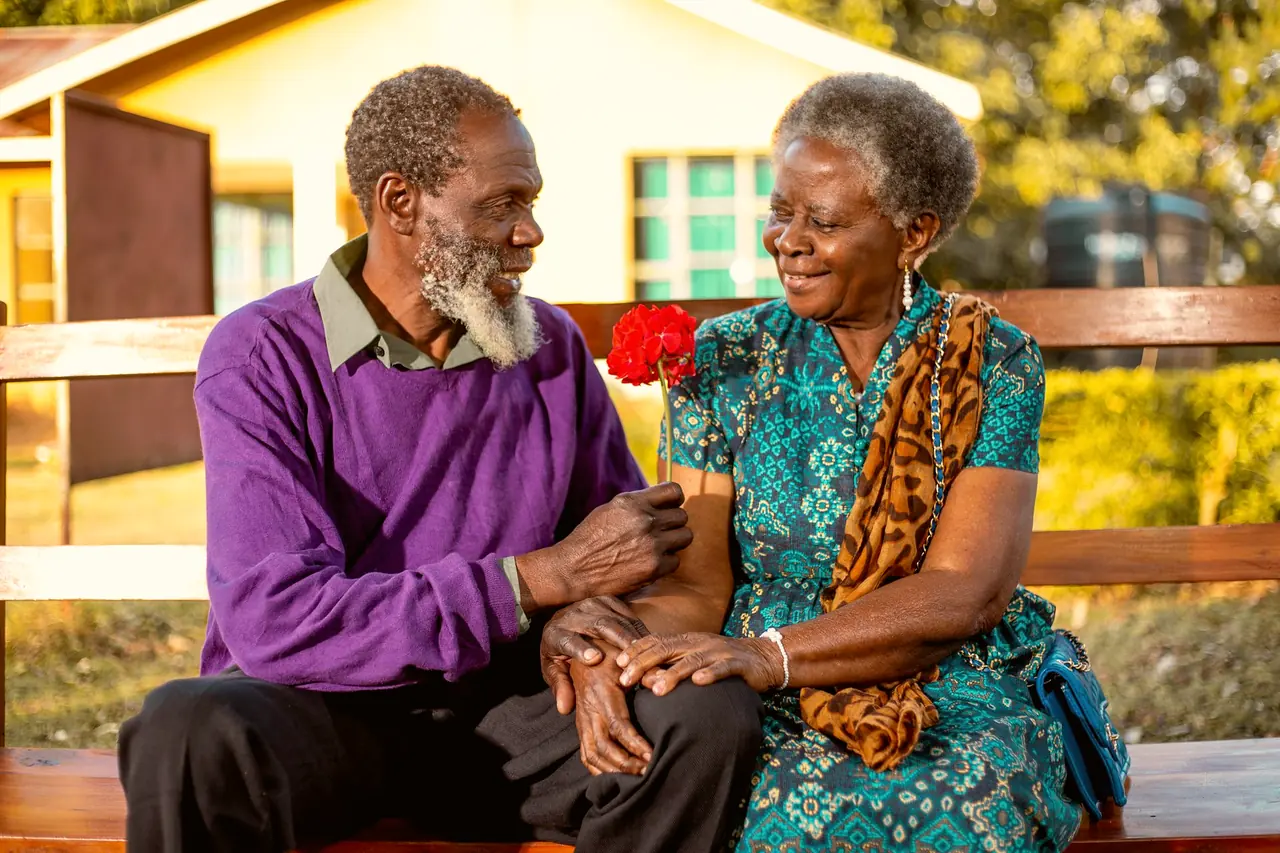 An older couple sitting on a bench in golden light